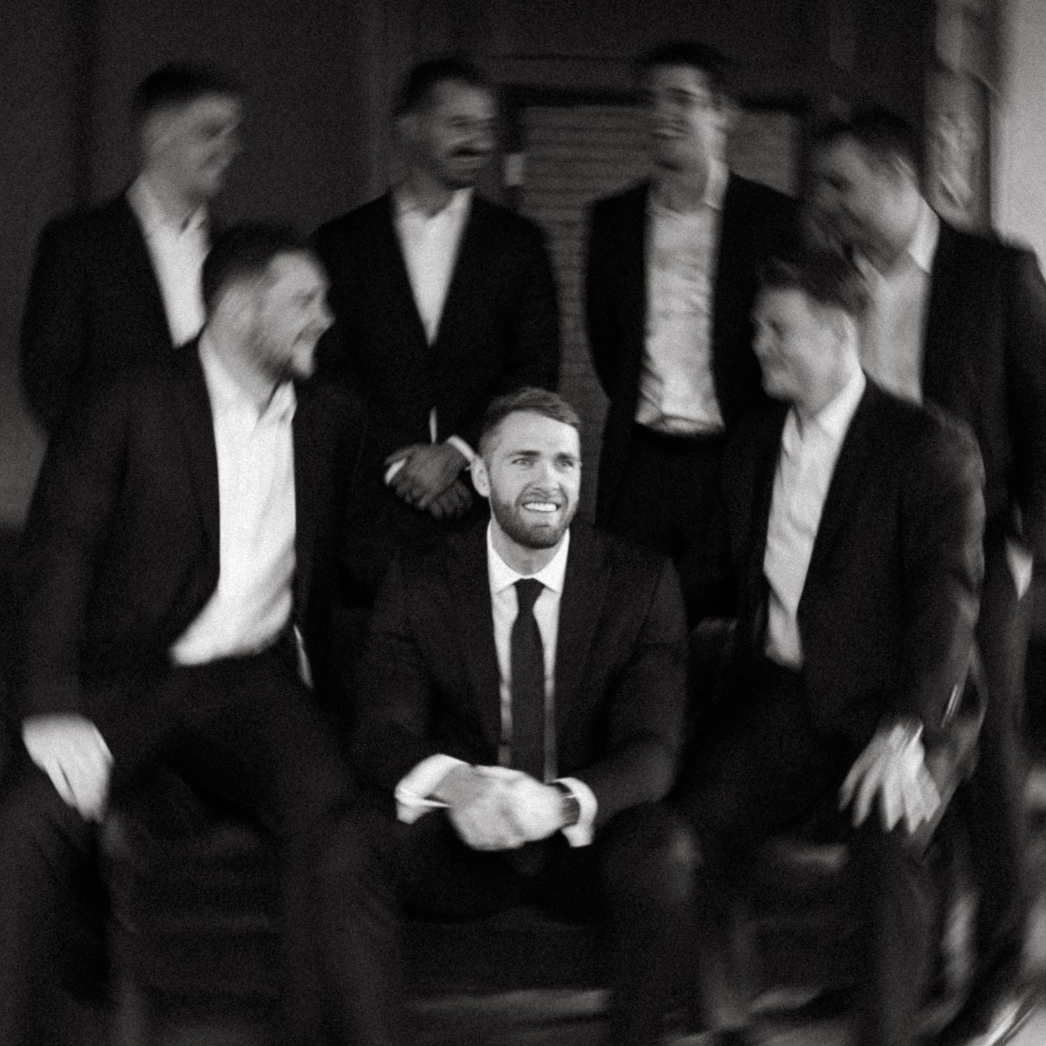Stylish groomsmen pose for creative motion blur photo in formal attire.