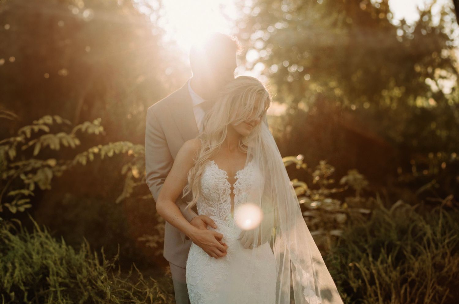 Romantic wedding couple embracing in a sun-drenched garden during golden hour.