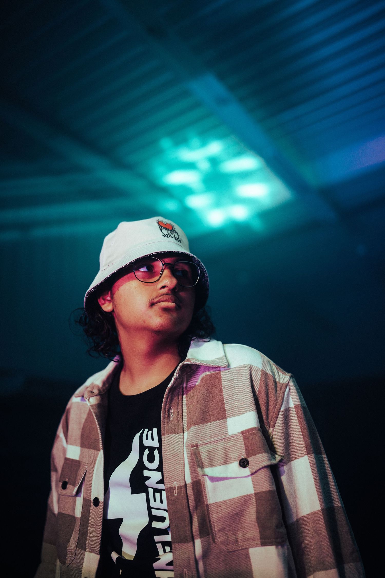 Person in a white cap and brown jacket illuminated by blue stage lighting.