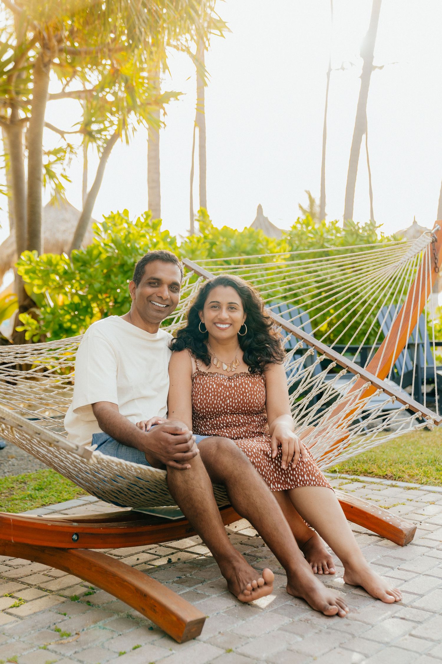 A couple relaxes together in a wooden hammock surrounded by palm trees and tropical foliage.