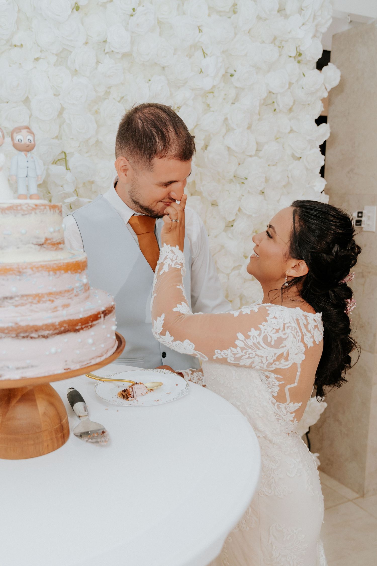 Couple in white wedding attire share an intimate moment against a textured white backdrop.