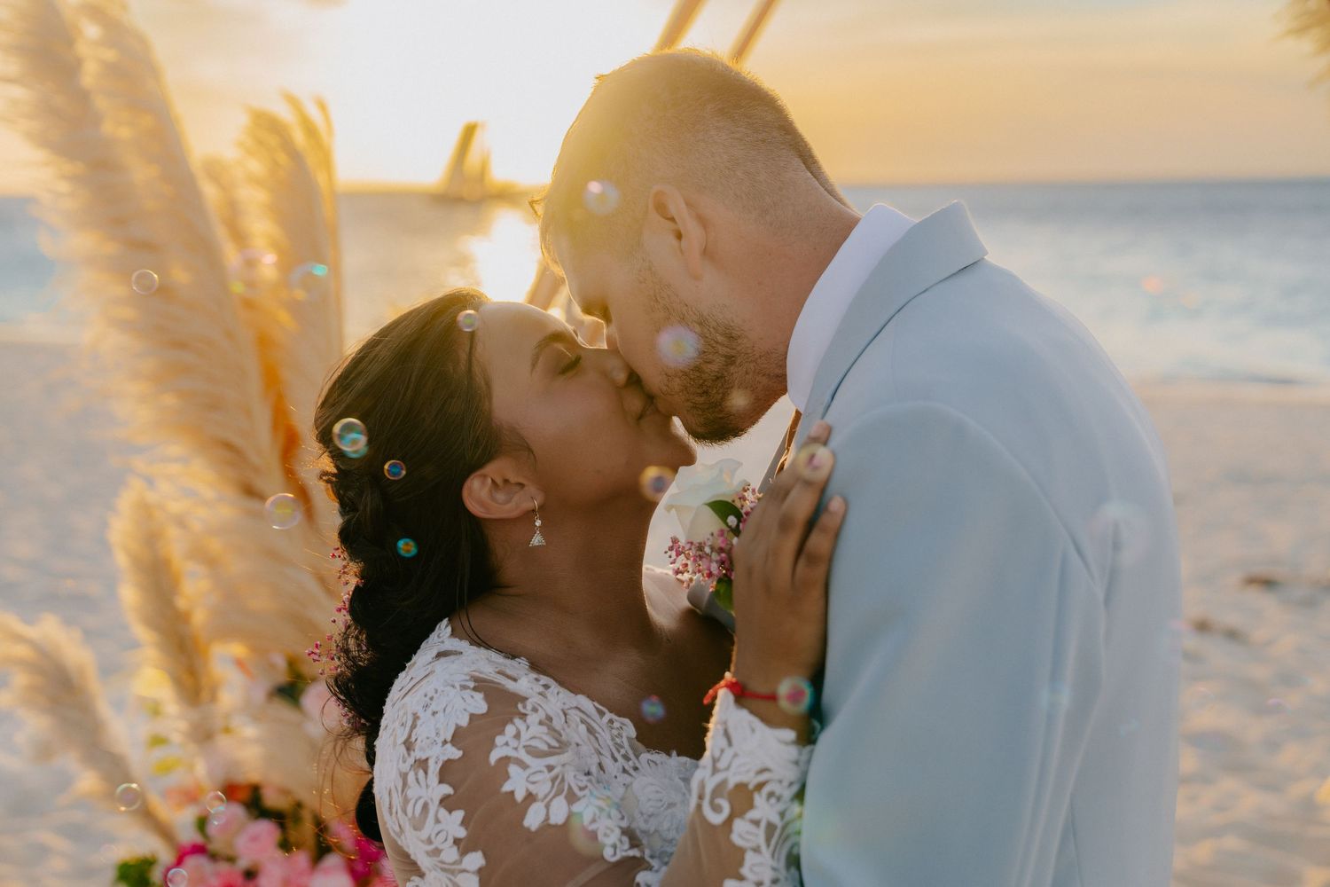 A romantic beach wedding scene at sunset with warm golden light filtering through palm trees and ocean waves in the background.