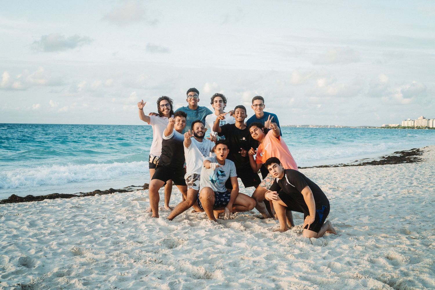 Group of friends relaxing together on a white sandy beach near turquoise waters.