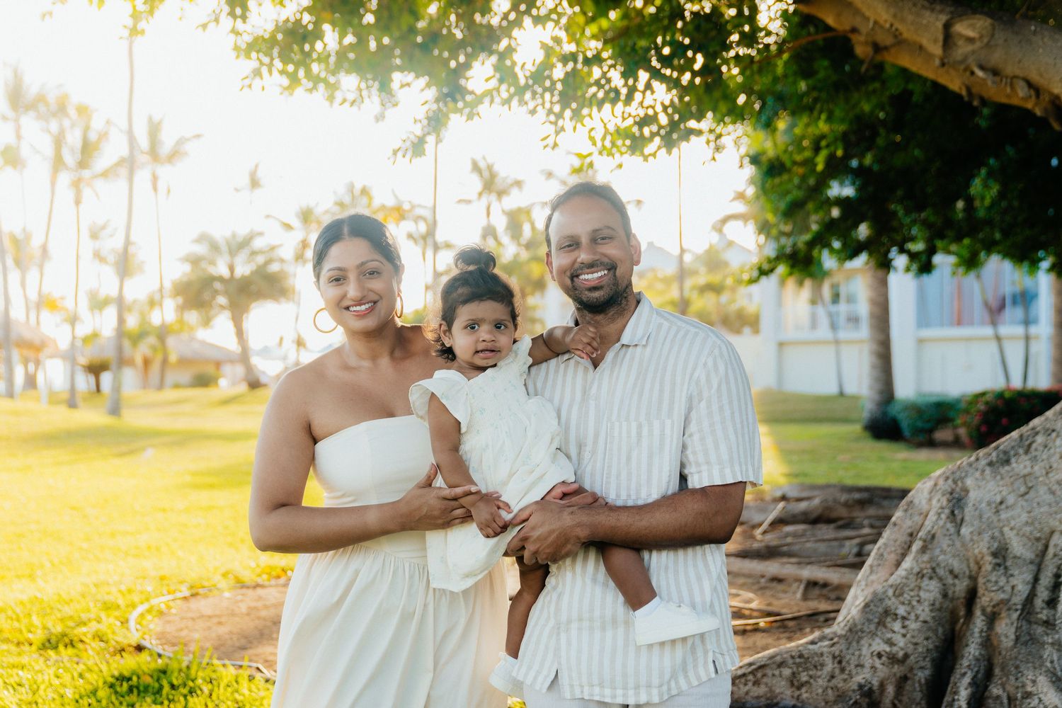 A family poses together on a sunny beach with palm trees in the background.
