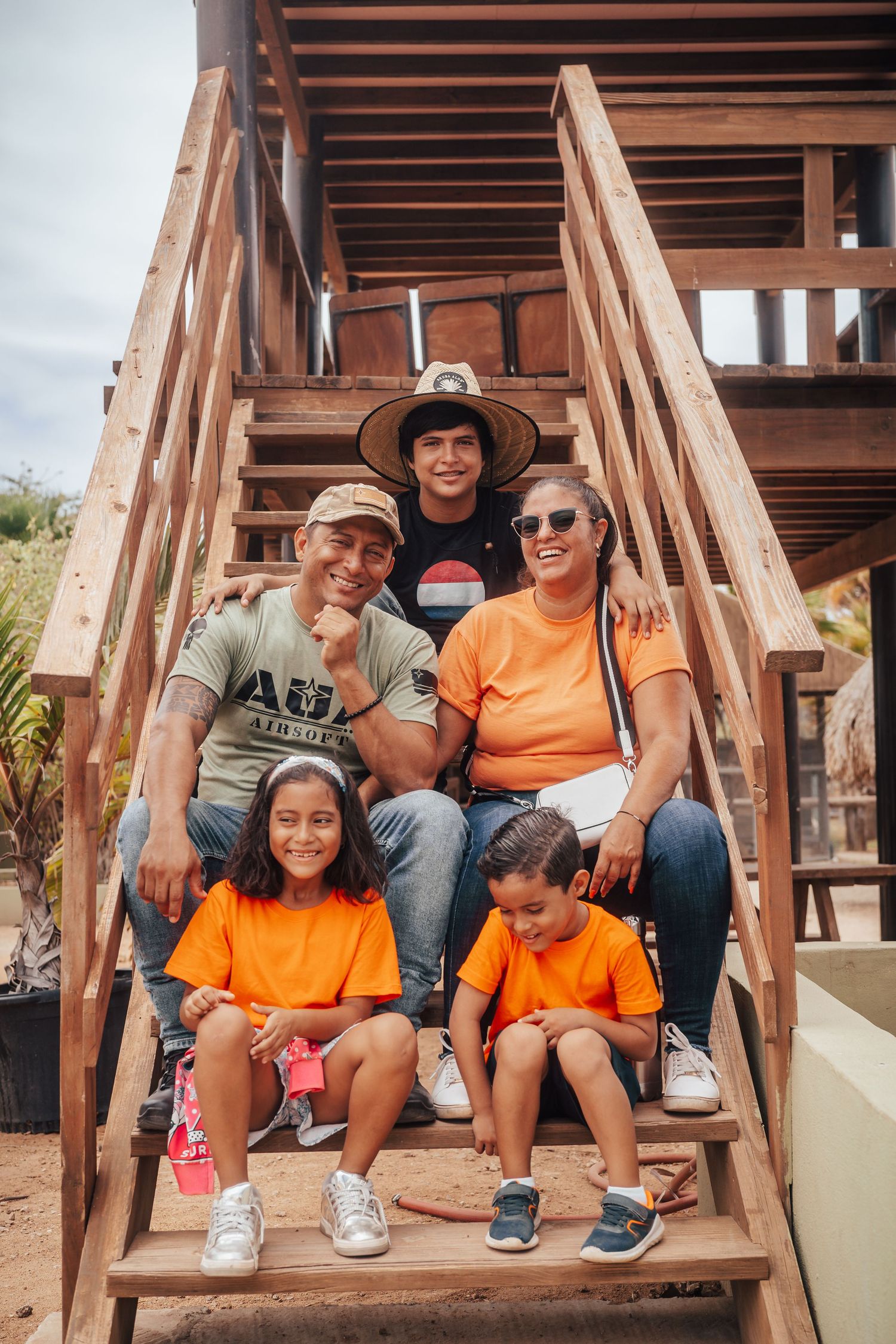 Group wearing orange t-shirts sitting on wooden stairs outdoors.