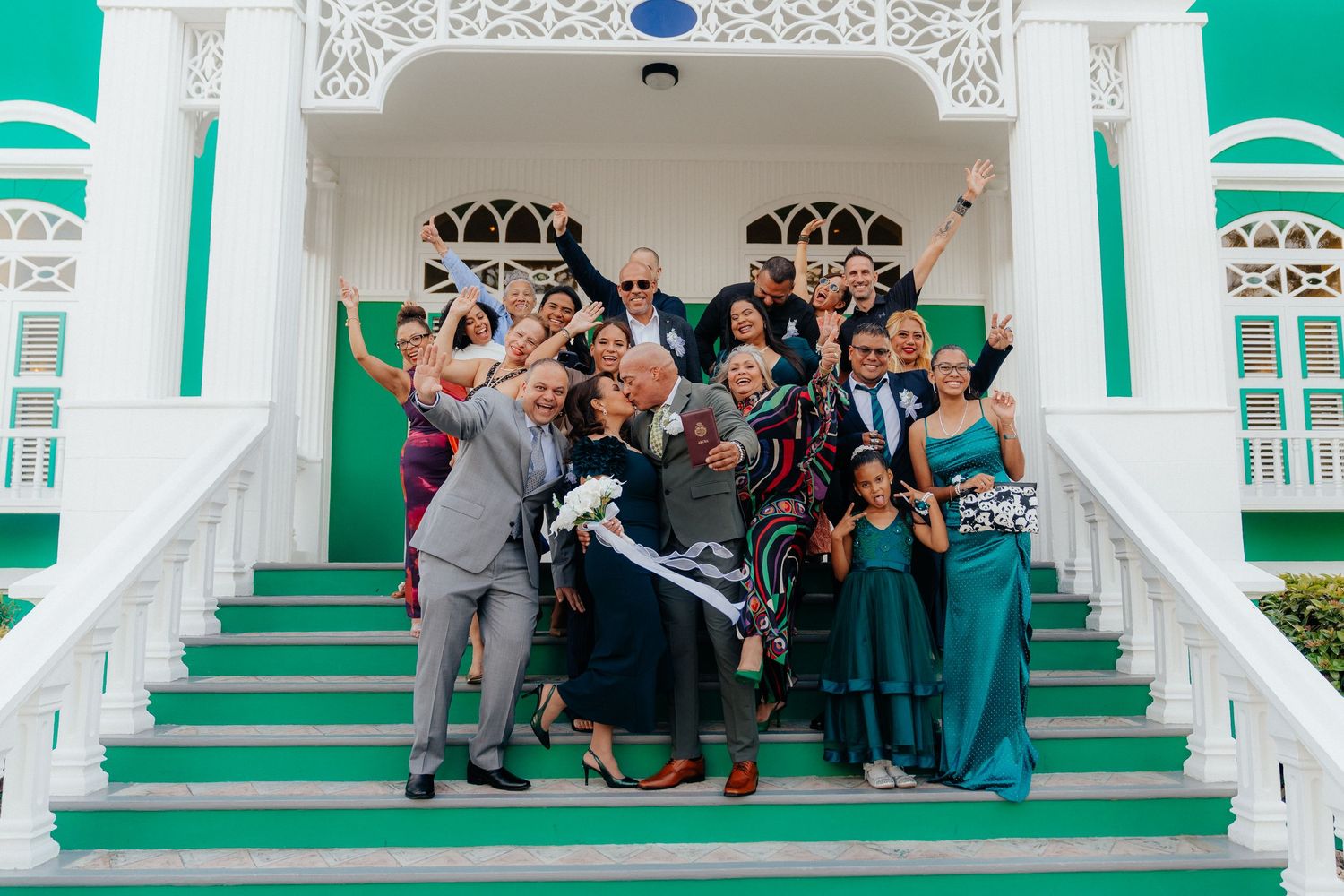 Wedding guests gathered on green and white steps of historic building for group photo.