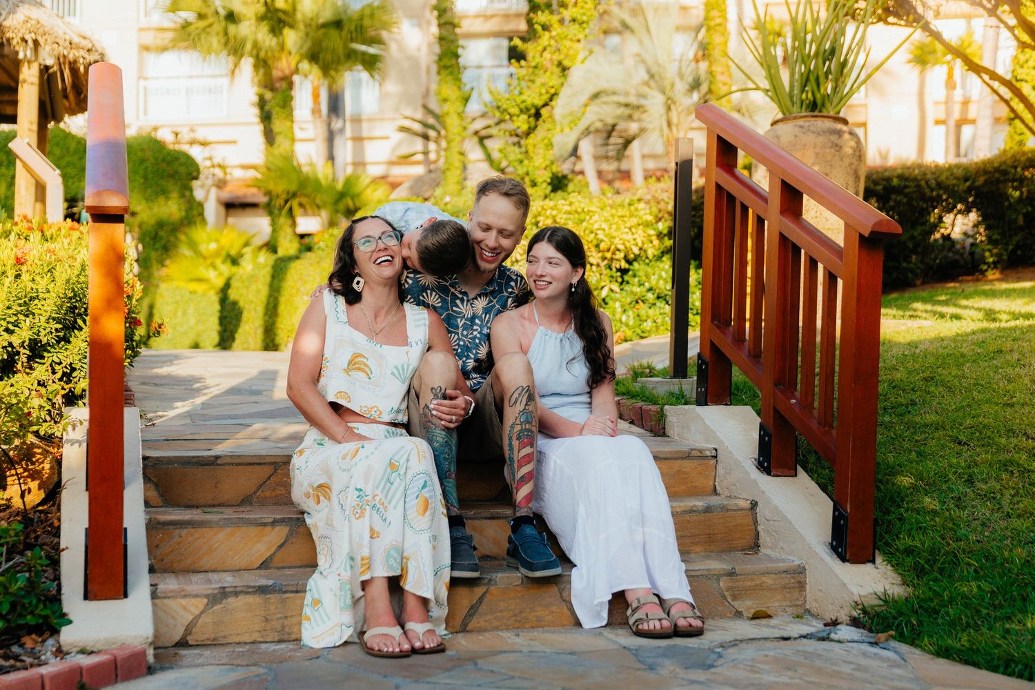 A group enjoying a sunny afternoon sitting together on outdoor stone steps surrounded by lush tropical landscaping.