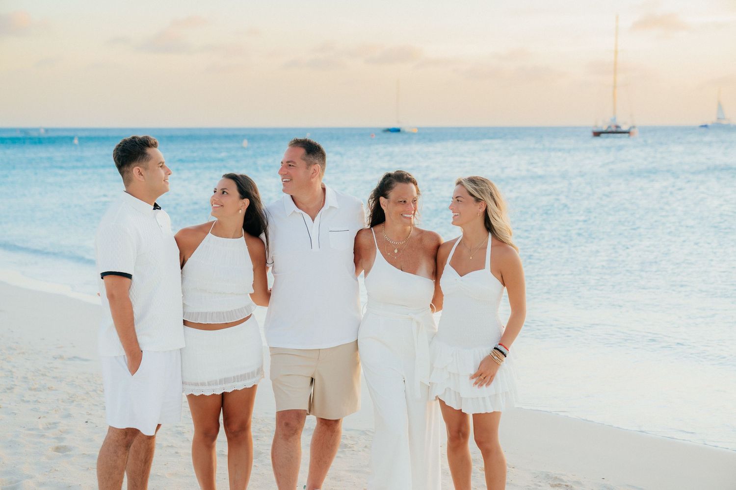 Group wearing coordinated white outfits walks along a scenic beach at sunset.