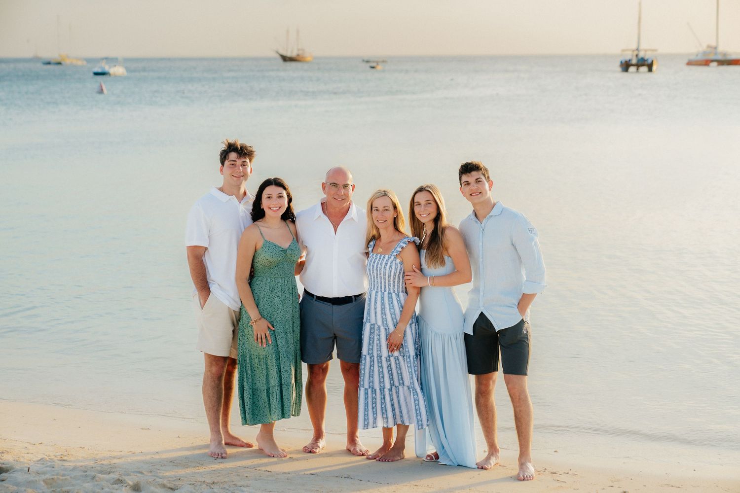 Extended family gathering on a tropical beach wearing coordinated blue and white outfits.