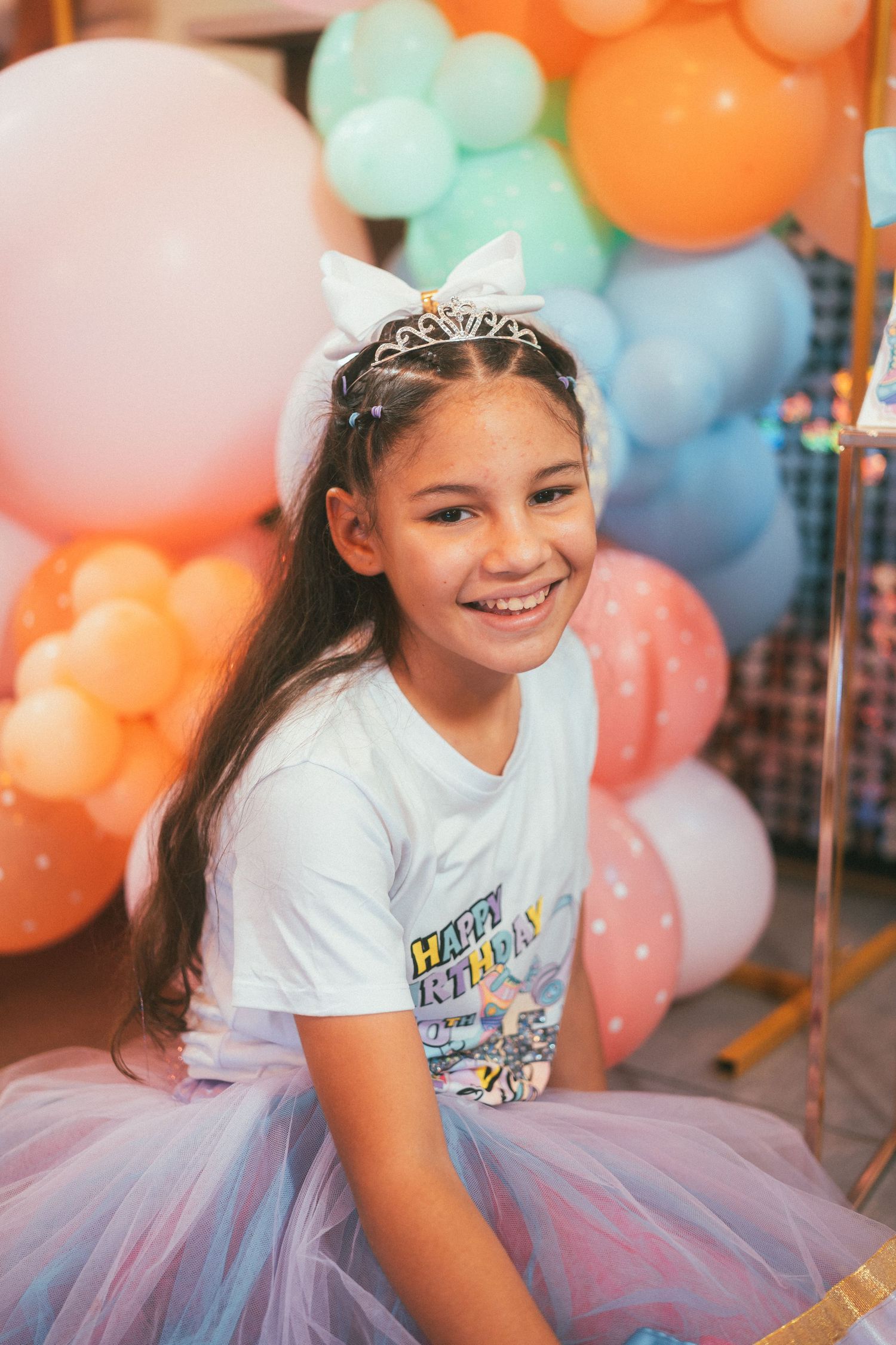 Young celebrant in tulle skirt surrounded by colorful balloon decorations.