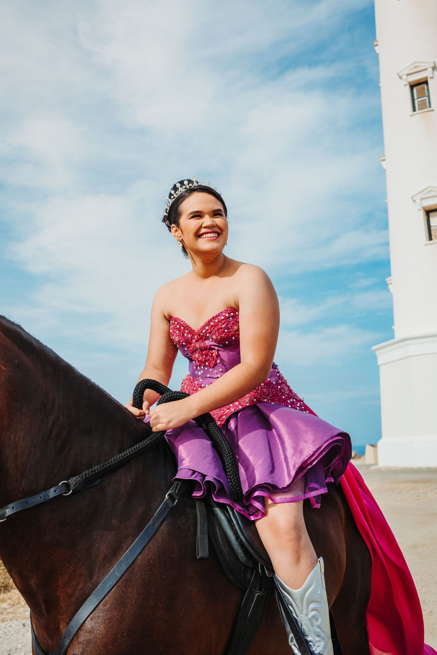 Person in a sparkly purple dress riding horseback near a white lighthouse.