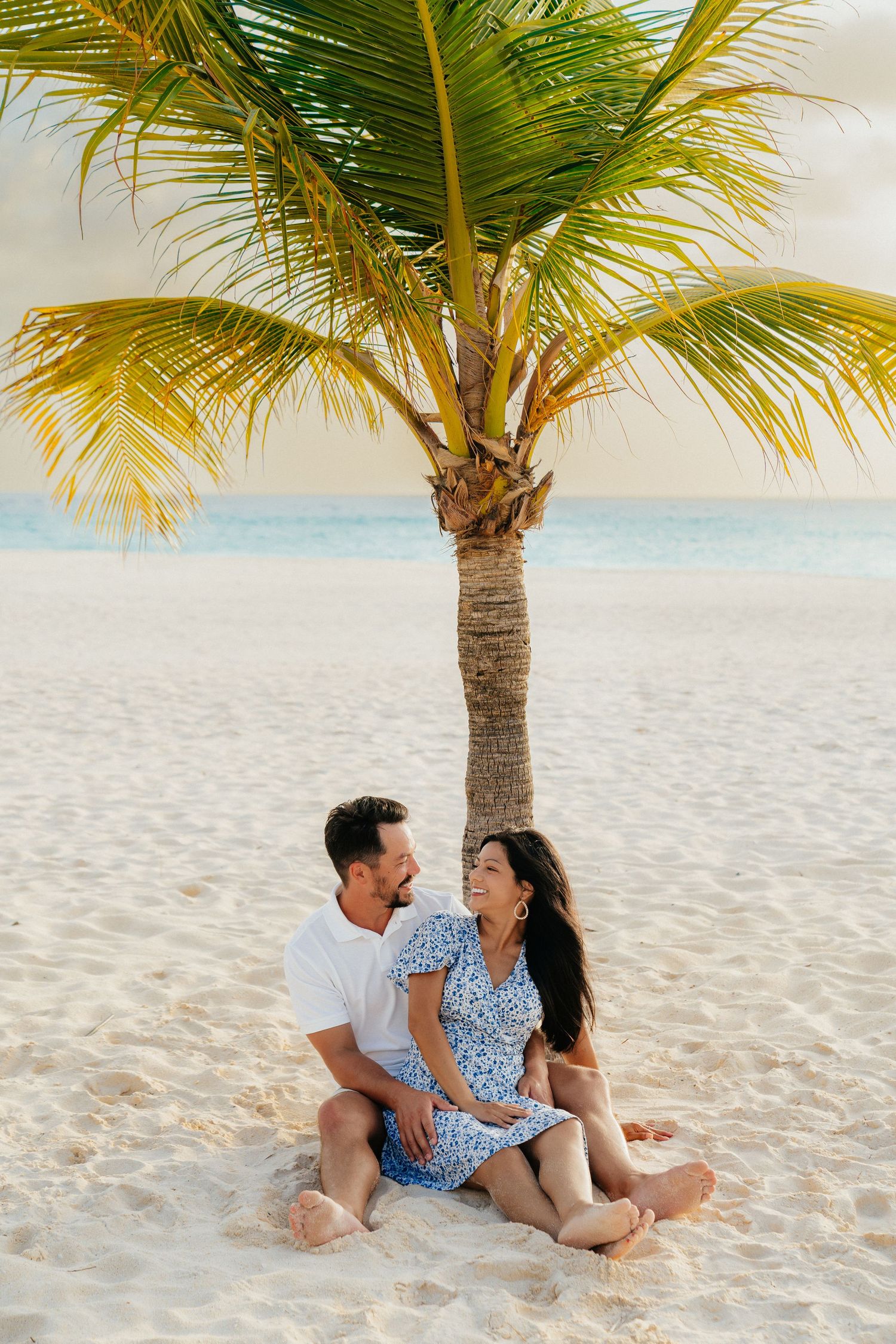 Couple relaxing under a palm tree on a pristine white sand beach.