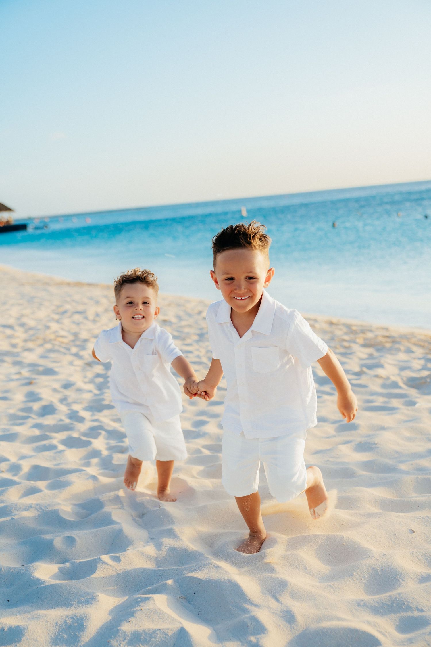 Children in white outfits play and run together on a pristine sandy beach.