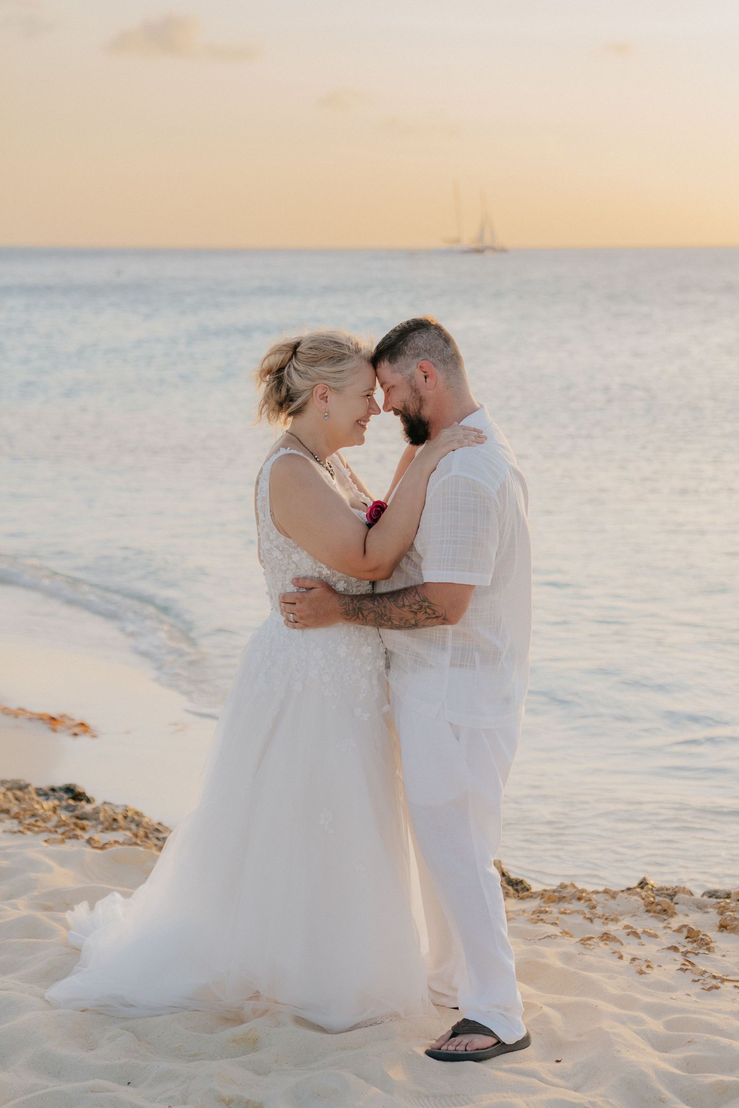 Intimate moment between newlyweds on beach during golden hour.