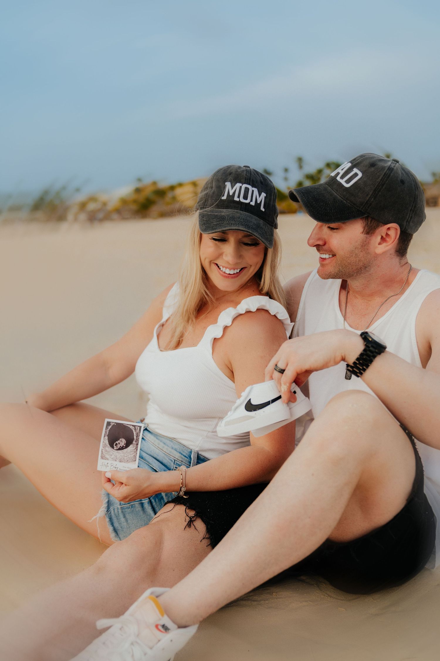 Couple wearing matching baseball caps relaxing on a sandy beach.