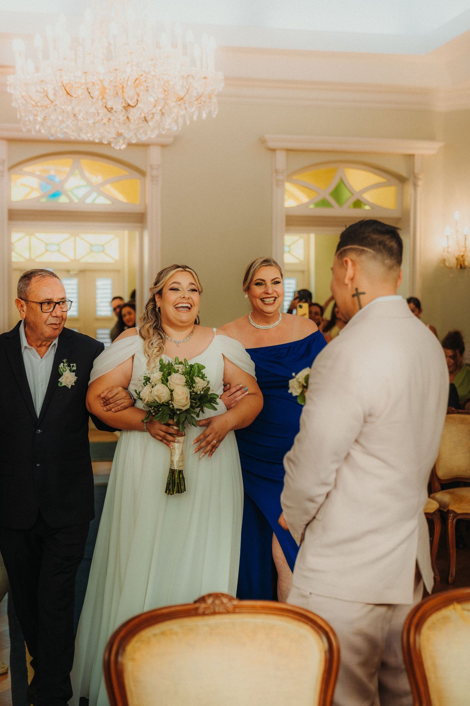 Wedding party members in pastel attire gather in elegant room with stained glass windows.