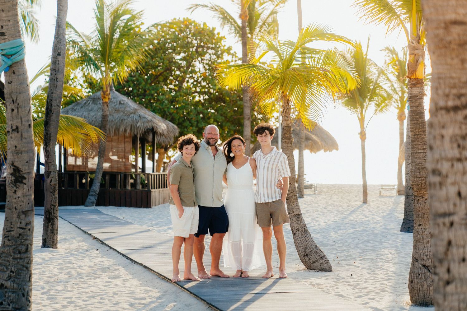 Group photo session on a sandy beach with palm trees during sunset.