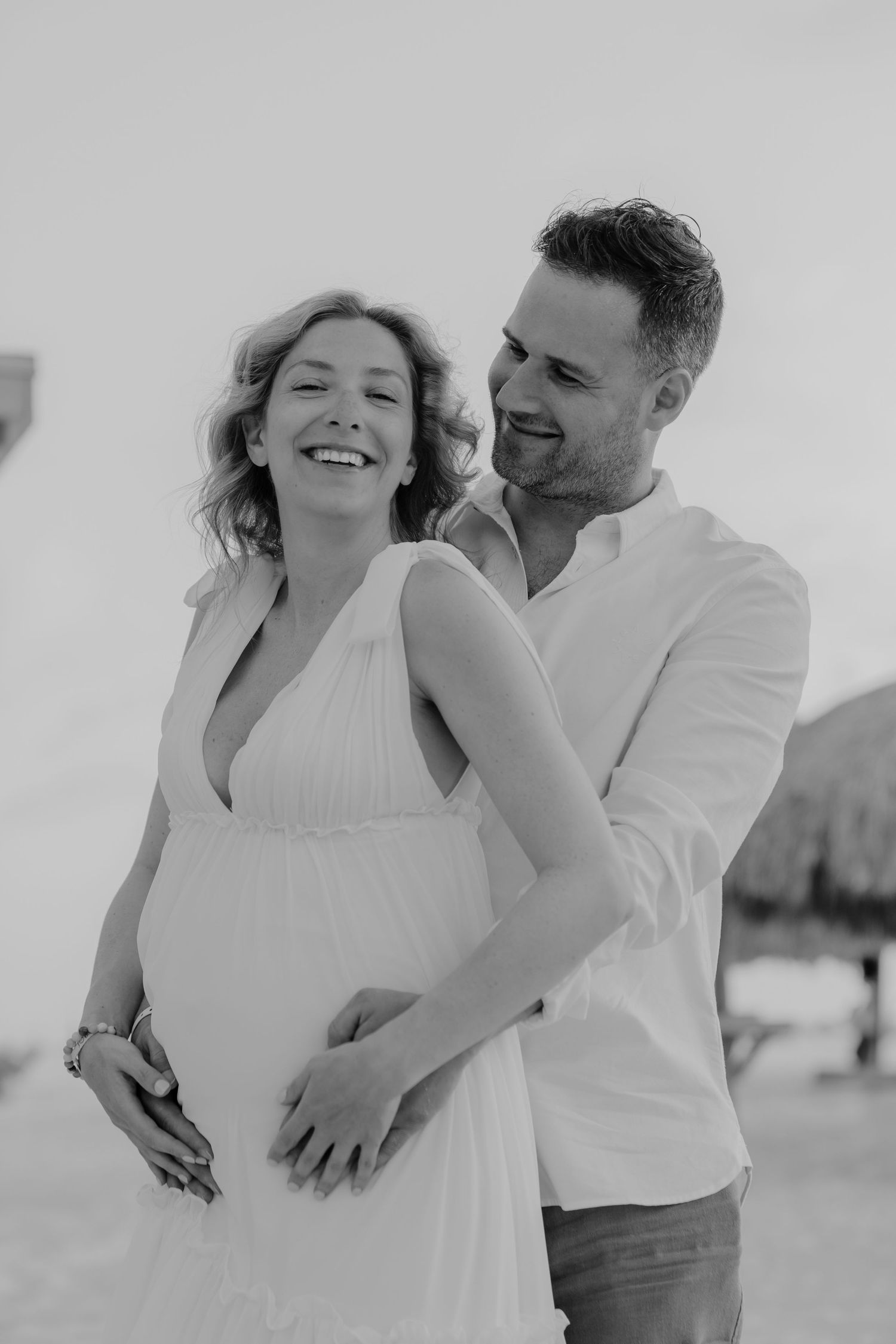 A couple in white clothing embraces and laughs joyfully together in a romantic black and white photoshoot series.