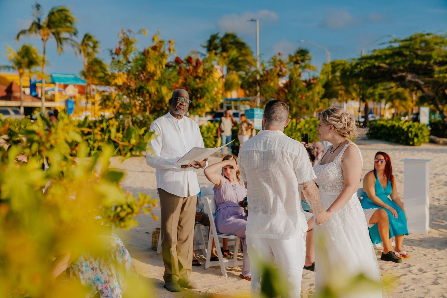 A beachside wedding ceremony with tropical foliage and palm trees in the background.