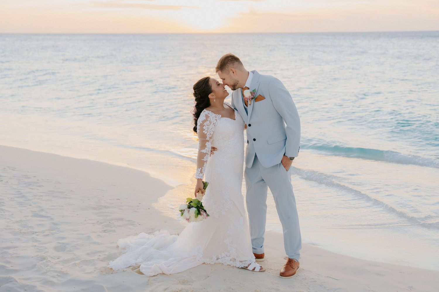 Newlyweds share intimate moments on a tropical beach at sunset.