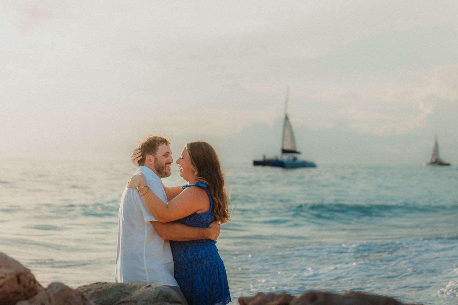 Romantic beach photoshoot with sailboats visible on the horizon at sunset.