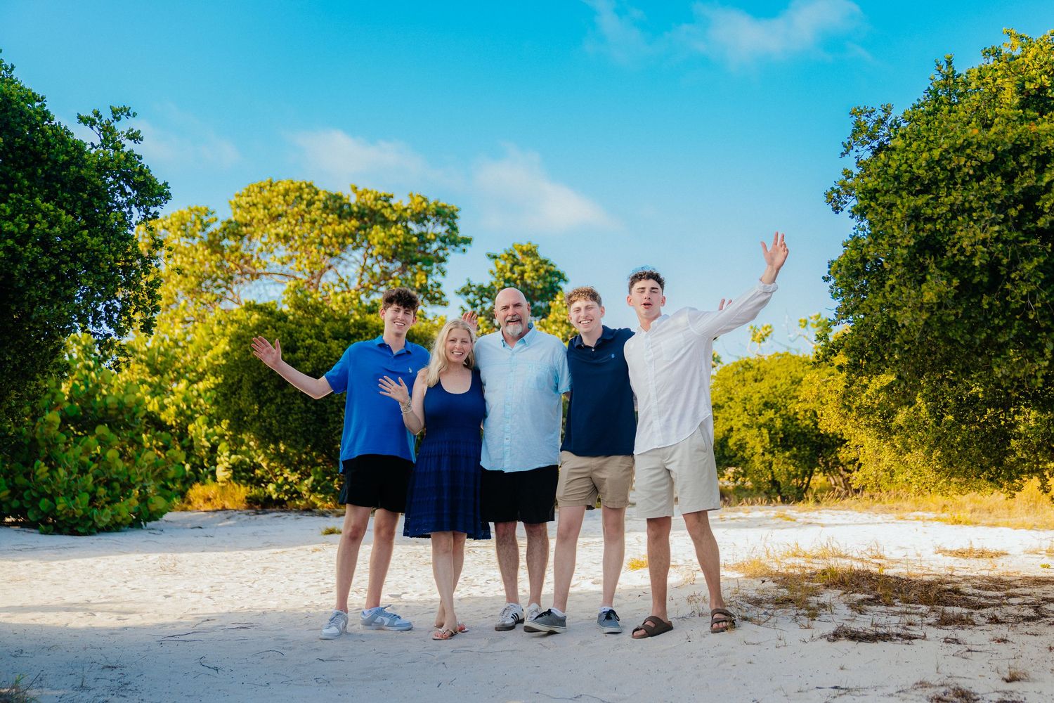 Family beach portrait session with tropical greenery and blue sky backdrop.