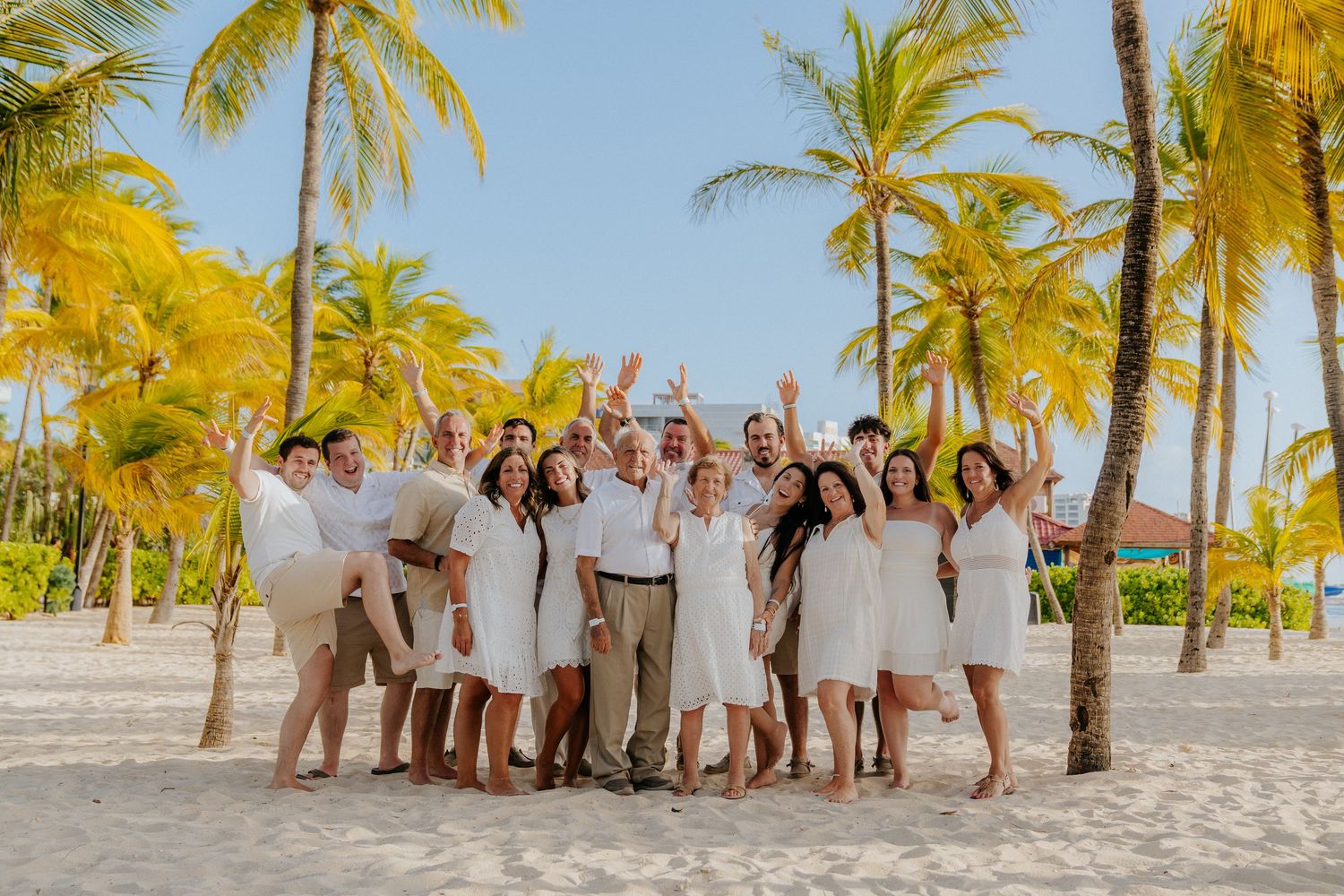 Large group poses for a fun beach photo with palm trees and white sand in the background.