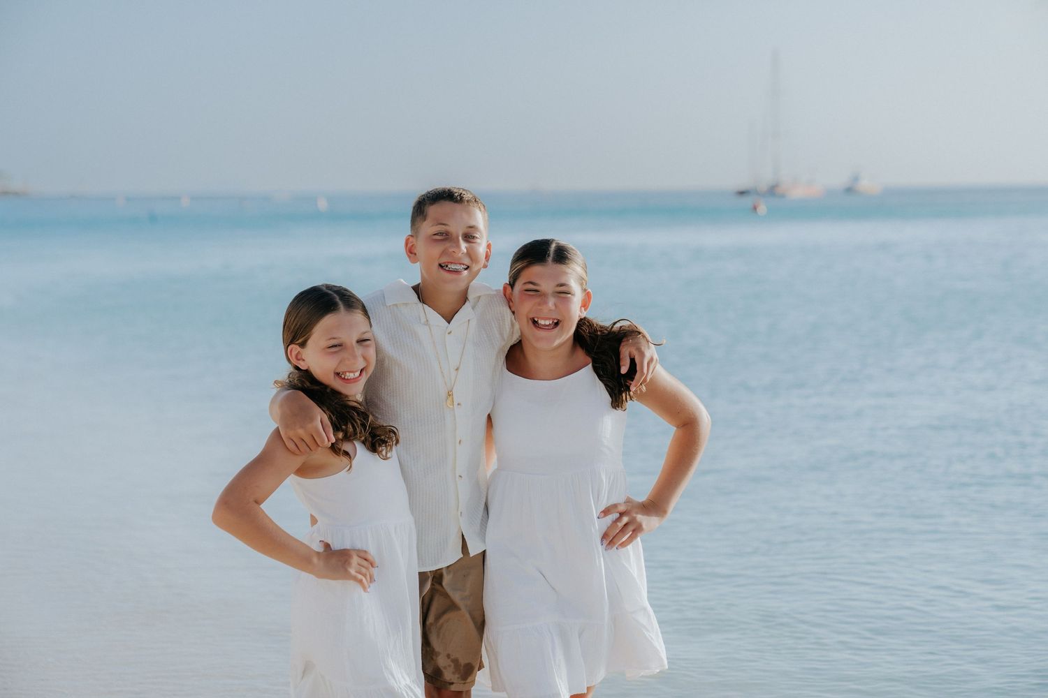 Three people pose together on a beach with turquoise ocean waters in the background.