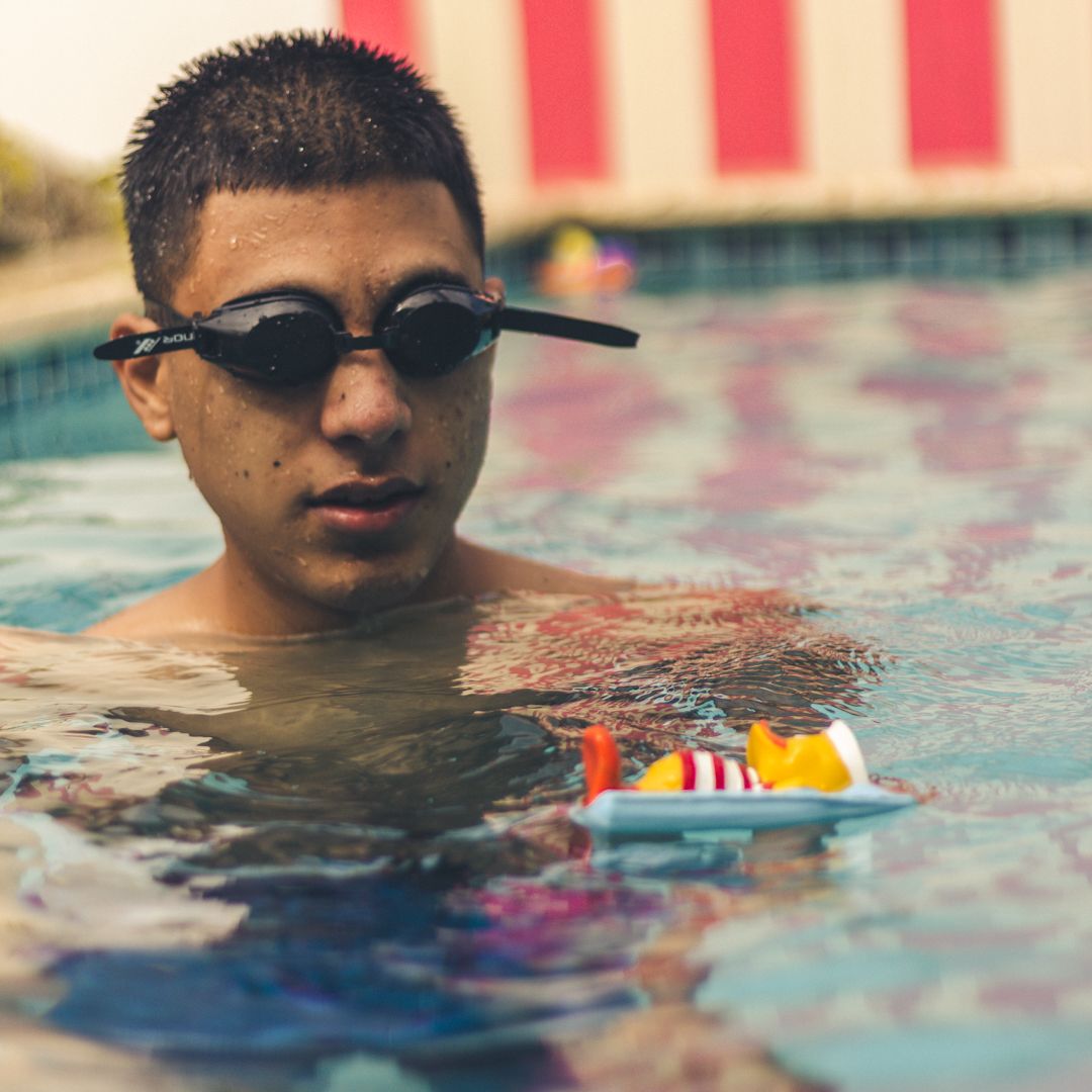 Close-up shot of person swimming in pool with colorful reflections on water surface.
