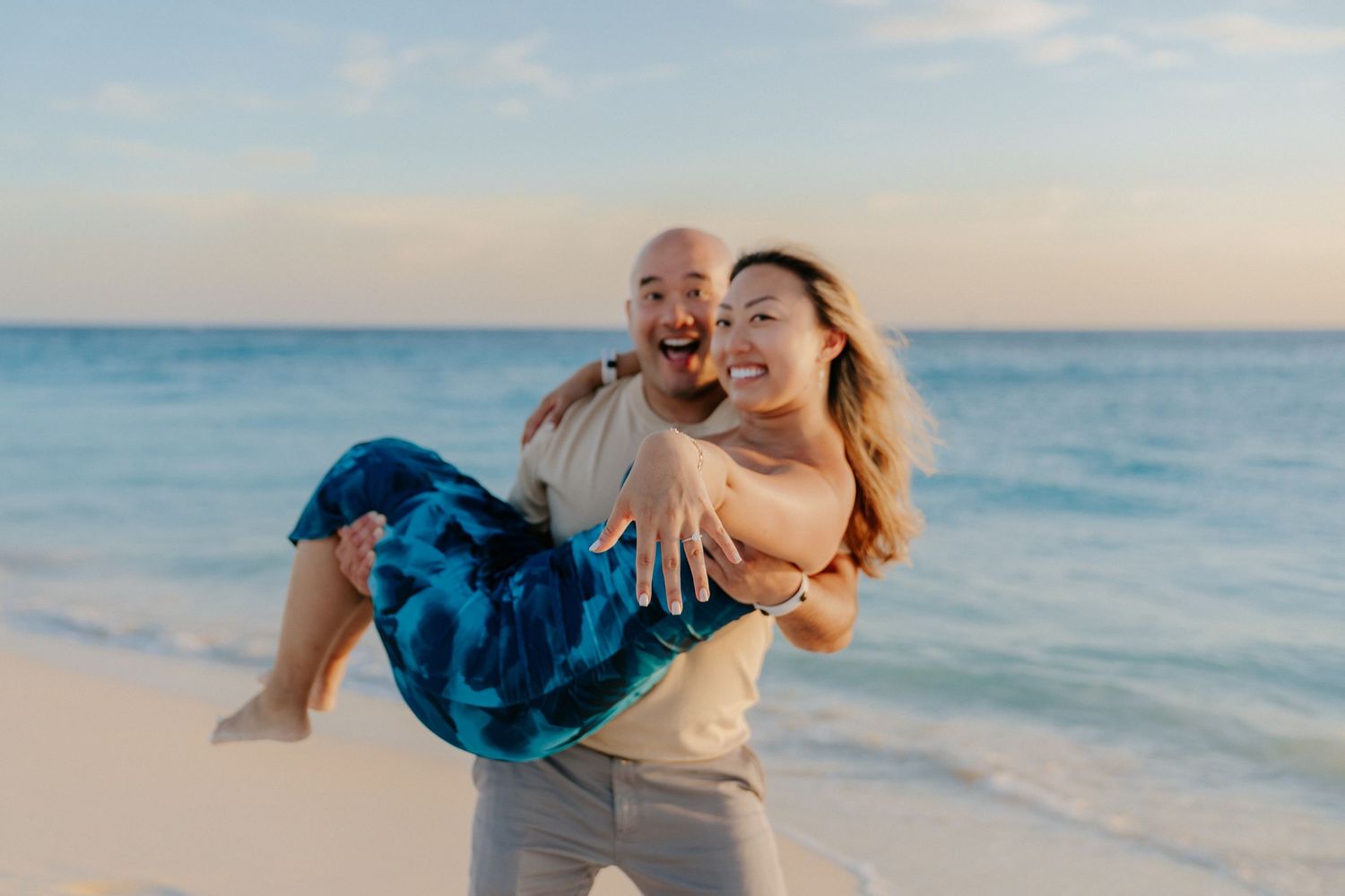 A playful moment captured on a beach at sunset as a couple enjoys a fun lift pose.