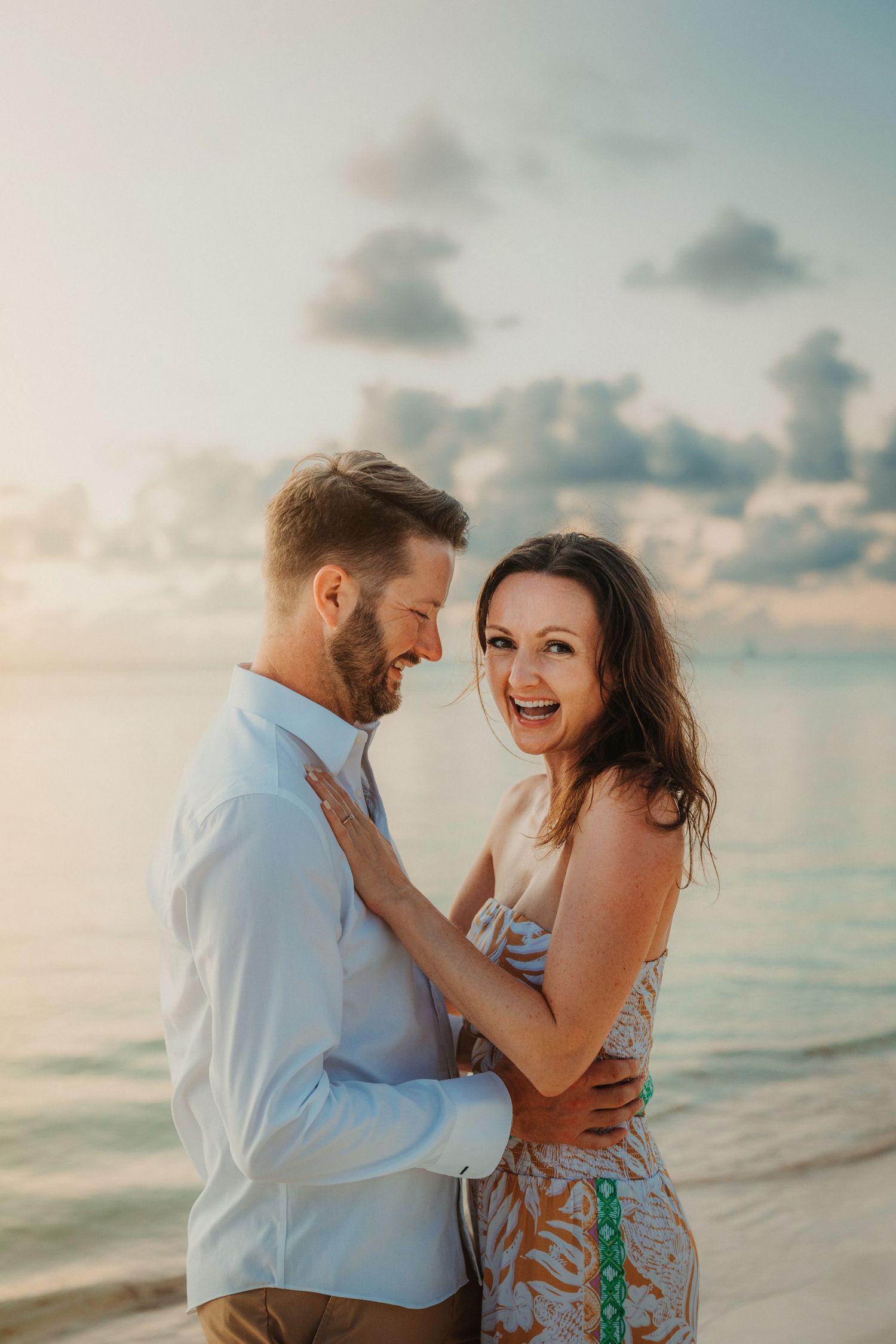 Joyful couple sharing playful moments during a beach photoshoot at sunset.