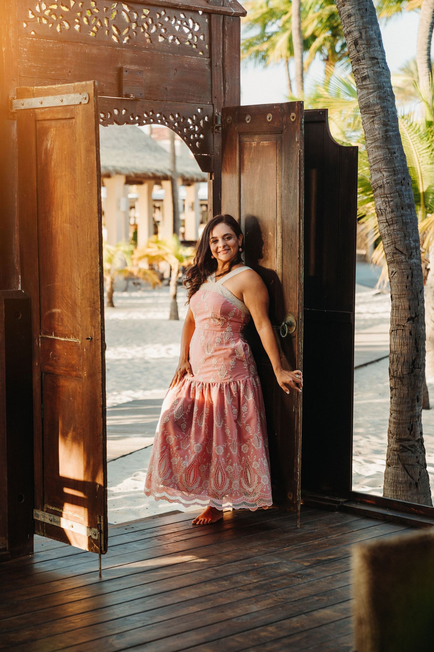 Woman in pink dress posing in rustic wooden beach cabana.