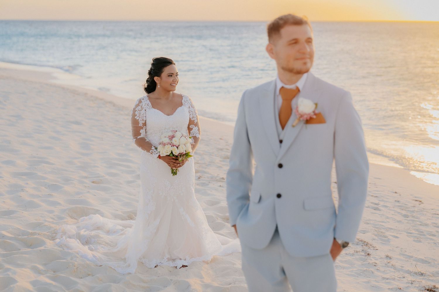 Elegant beach wedding photos of couple in white attire walking along shore.