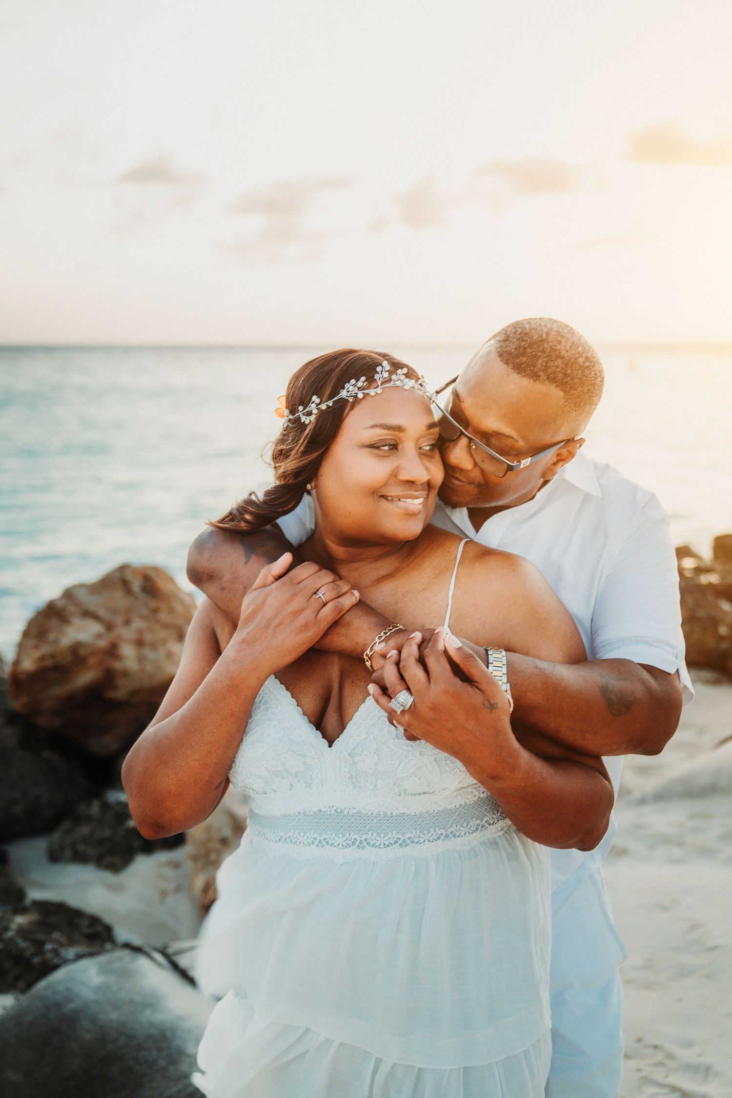 A couple shares intimate moments on a rocky beach during sunset.