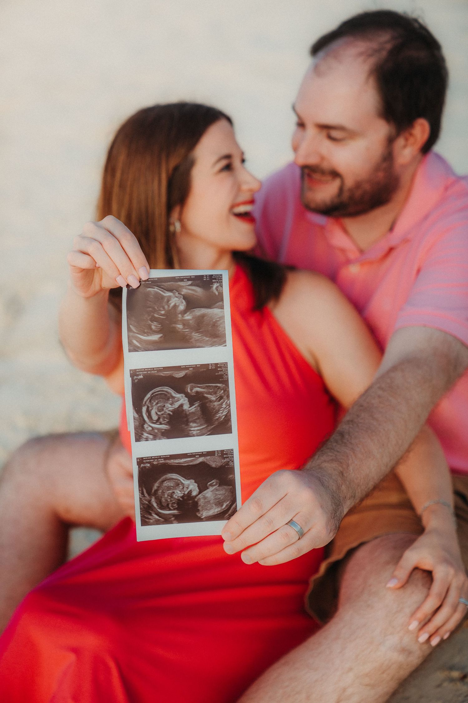 Couple holding ultrasound photos while sitting together outdoors.