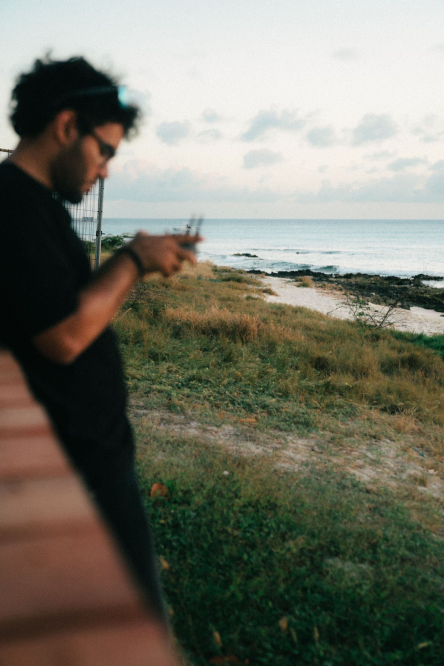 A silhouetted figure stands on a coastal path overlooking the ocean at dusk, with grassy terrain in the foreground.