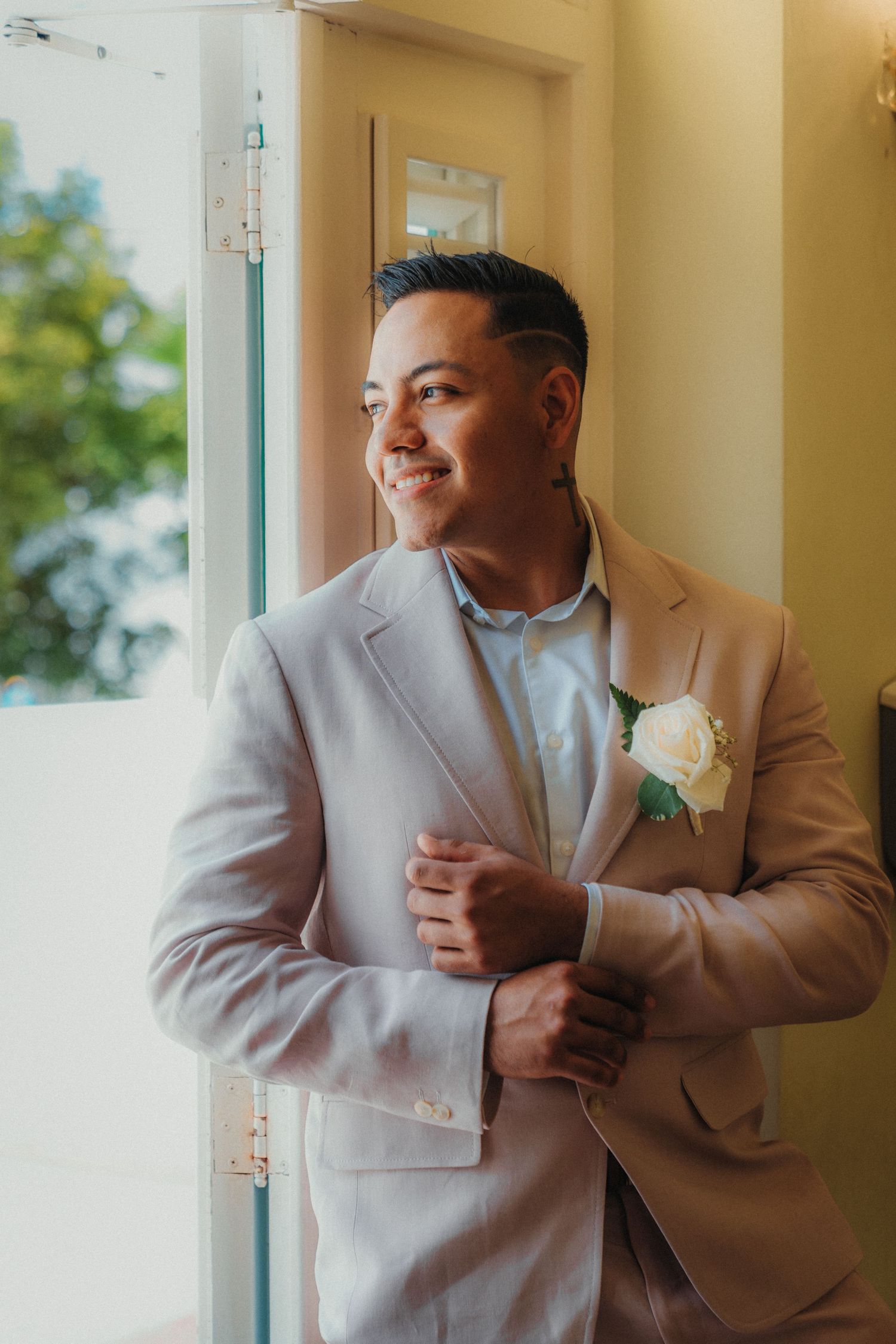 Person in light gray suit jacket stands by window in warm lighting.
