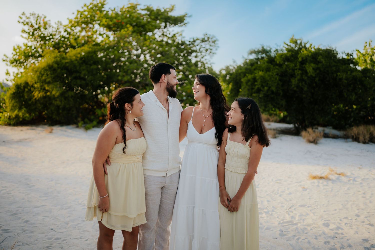 Bride and groom with two bridesmaids in yellow dresses on a sandy beach at golden hour.