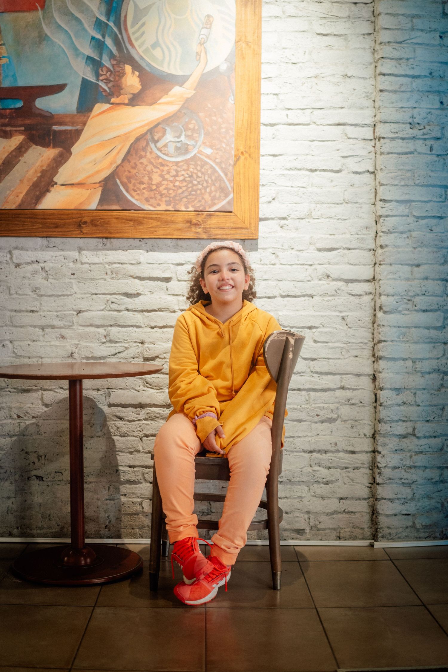 Person in yellow hoodie sitting against white brick wall.