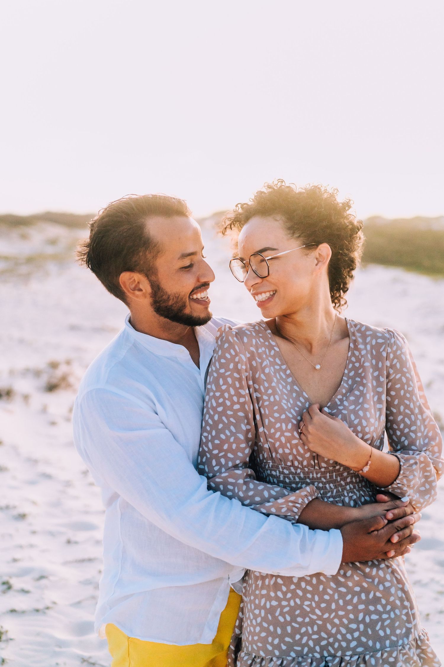 A couple laughing and embracing on a sandy beach during golden hour.
