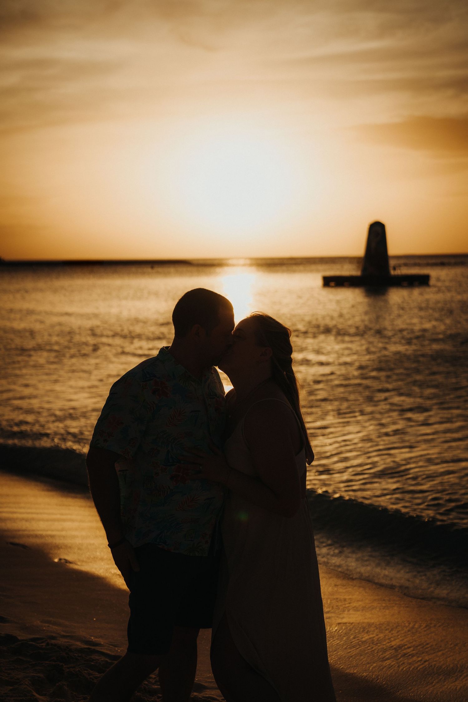 Silhouettes of people on beach at sunset with boat visible on horizon.