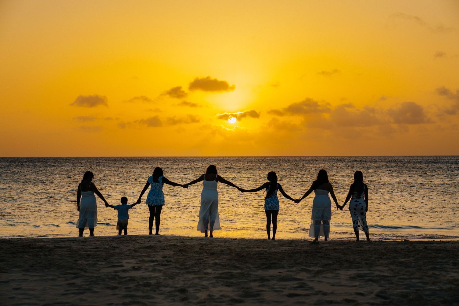 Silhouettes of people holding hands against a dramatic orange sunset over the ocean.