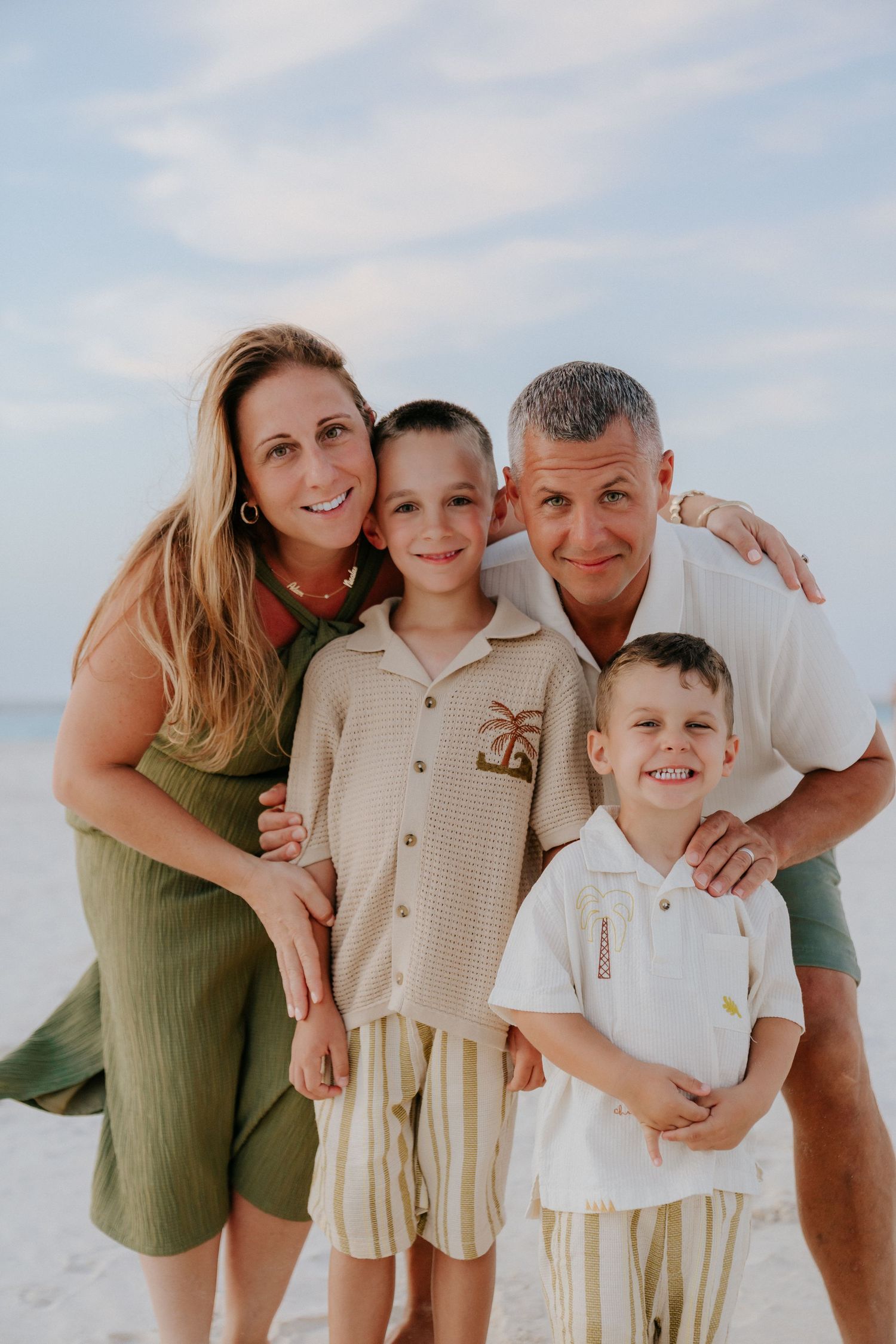 A casual beach portrait series of people in coordinating outfits against a blue sky background.