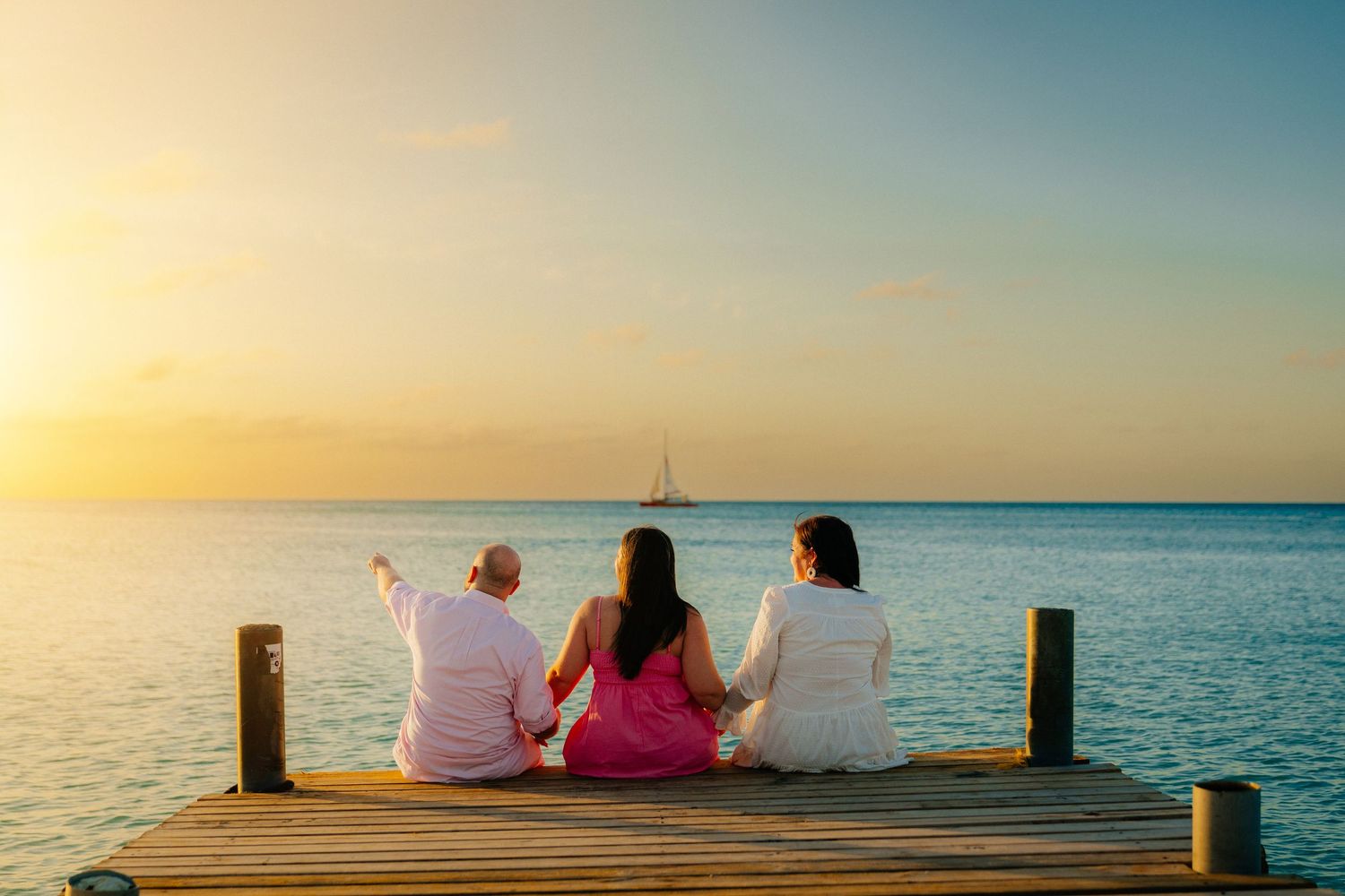People sit together on a wooden dock overlooking a calm ocean at golden hour.