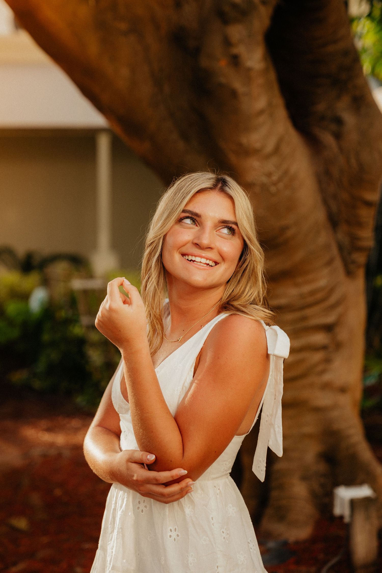 Woman in white dress posing playfully near palm trees outdoors.