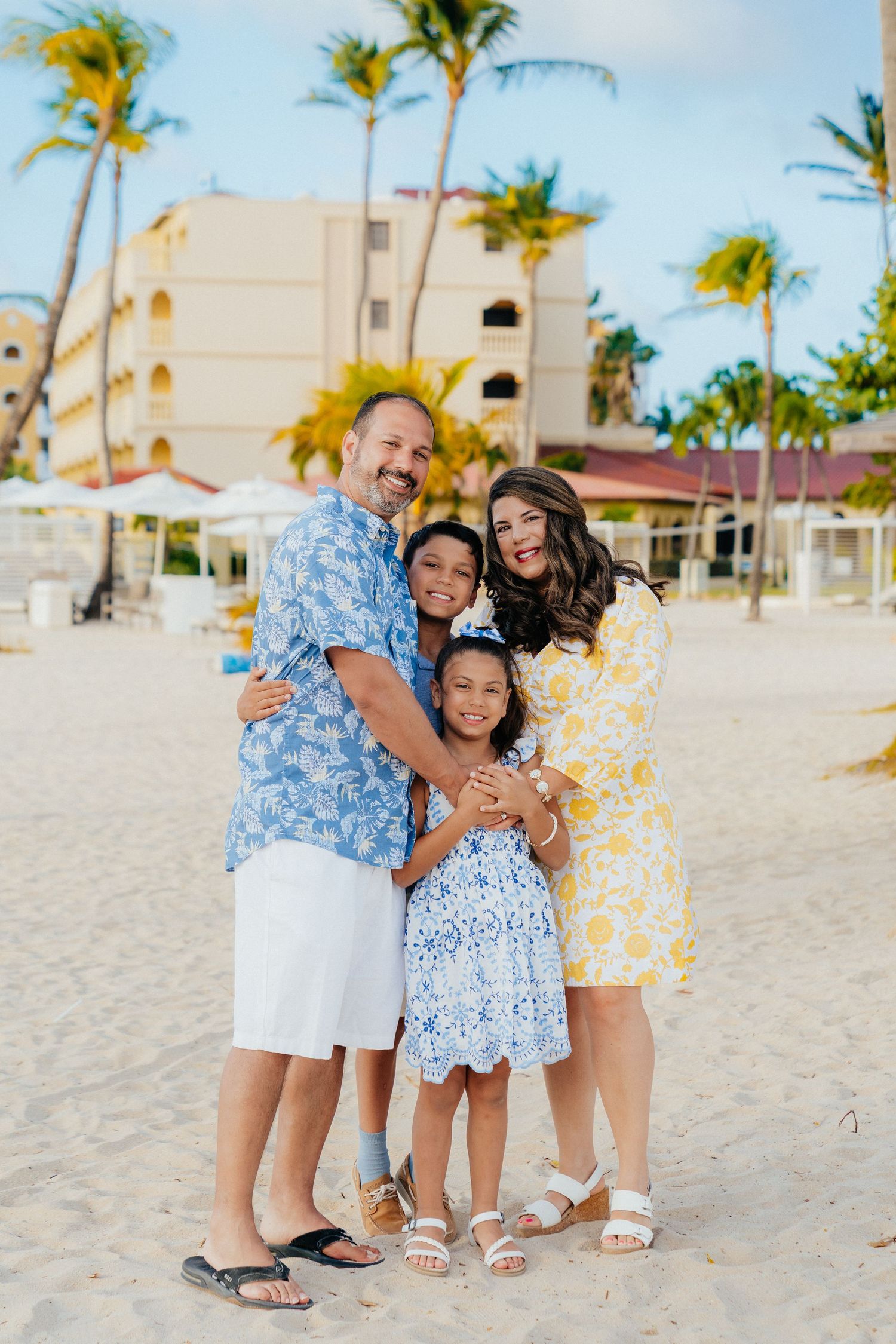 Family group wearing coordinated blue and yellow outfits playing together on a sandy beach.