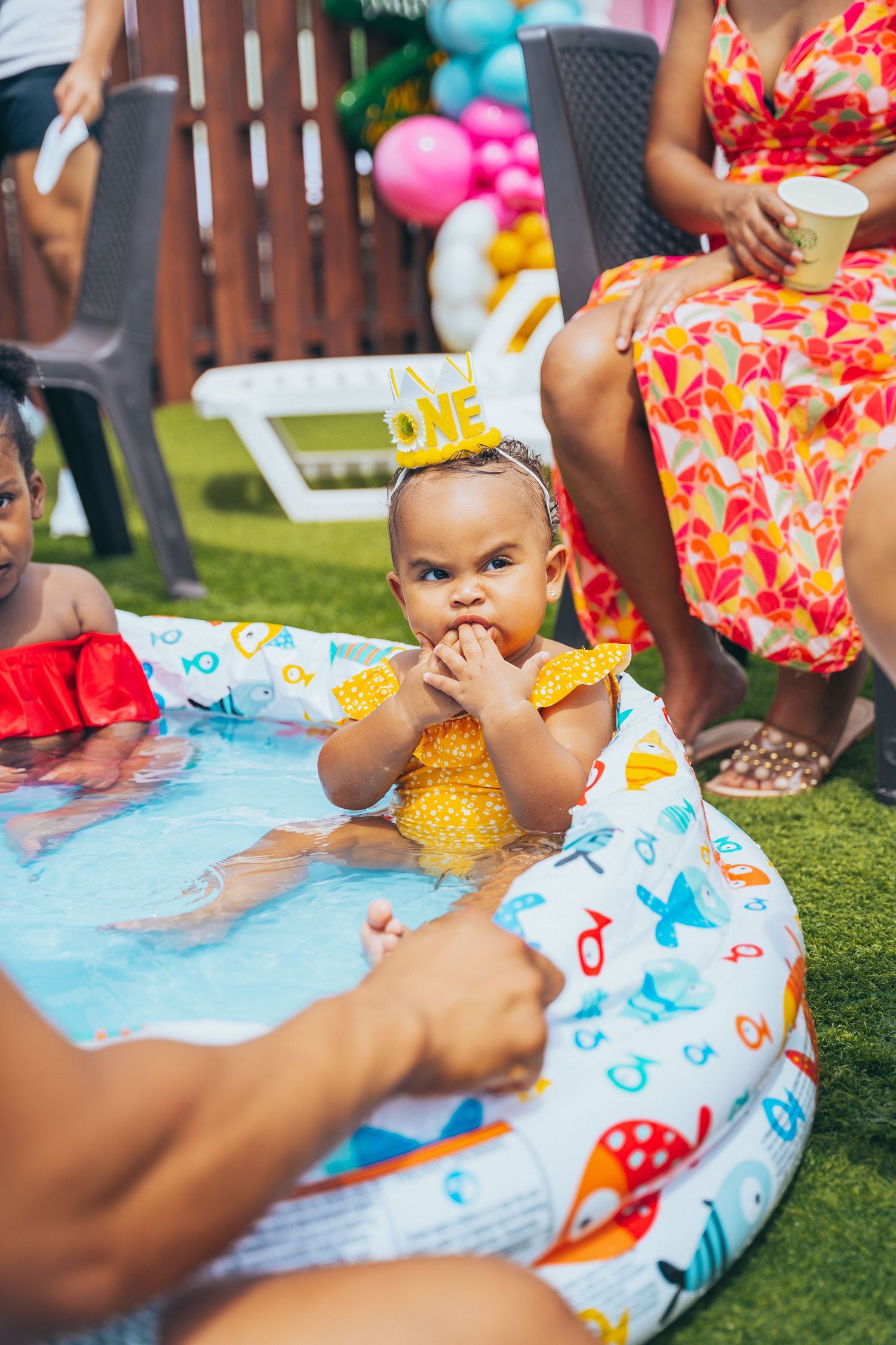 Baby playing in inflatable pool with colorful toys during outdoor summer party.
