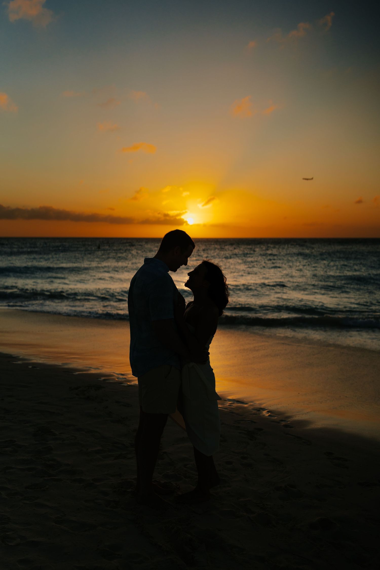 Two silhouettes embrace on a beach against a vibrant orange sunset over the ocean.