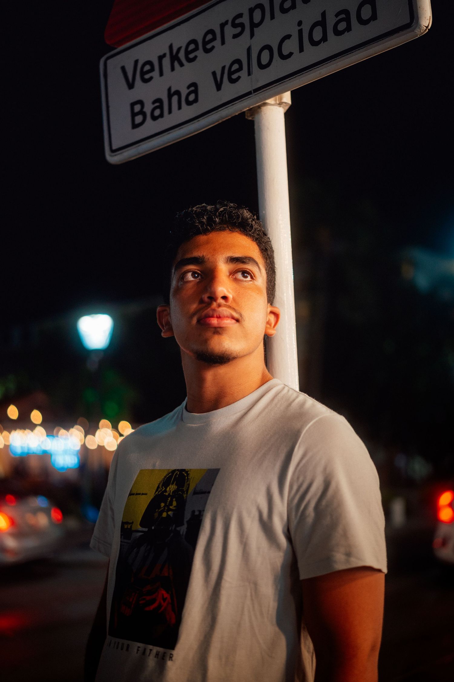 Person in white t-shirt standing under street sign at night.