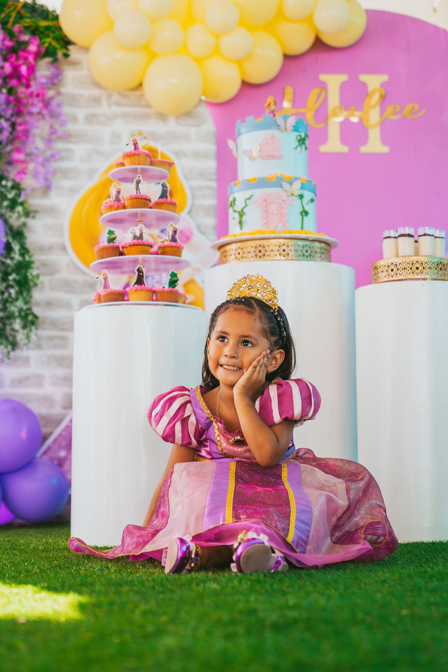 Decorative birthday setup with white pedestals, yellow balloons, and pink accents on artificial grass.